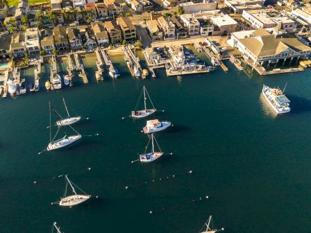 Aerial view of a coastal town with a marina full of boats, a pier extending into calm blue water, and an orderly grid of houses along the shore.