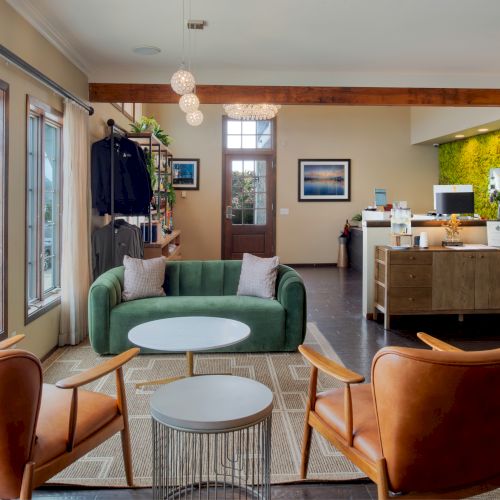 Cozy living room with a sofa, coffee table, and armchairs; a doorway leads to a bright kitchen in the background.