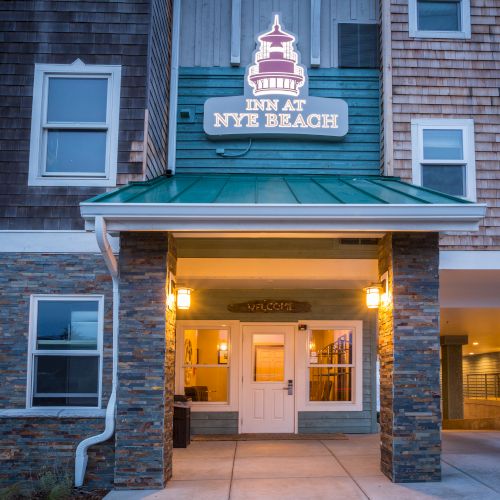 A brick building with a lit entrance, two banners, and a blue sign above the door. The doorway glows warmly from inside.