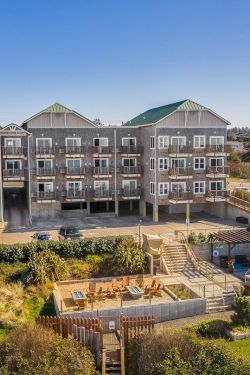 A row of coastal-style multi-story homes with balconies, a fenced backyard with a pool, and landscaped outdoor living spaces under a bright blue sky.