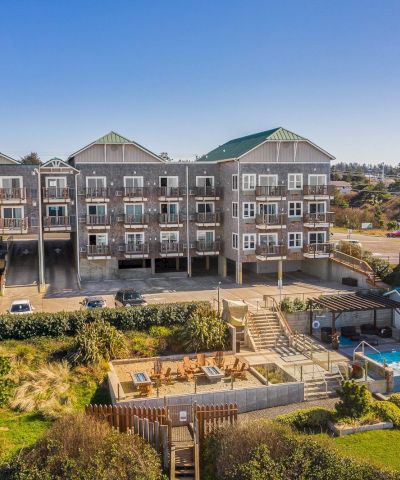 A row of coastal-style multi-story homes with balconies, a fenced backyard with a pool, and landscaped outdoor living spaces under a bright blue sky.