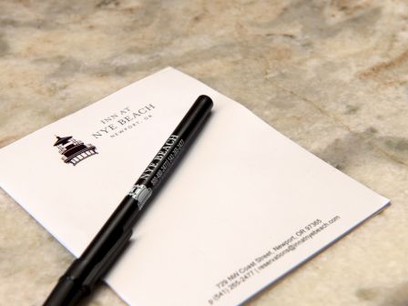 A black marker lies on a white card on a light stone surface, with a small illustration and text at the top left, plain and minimal.