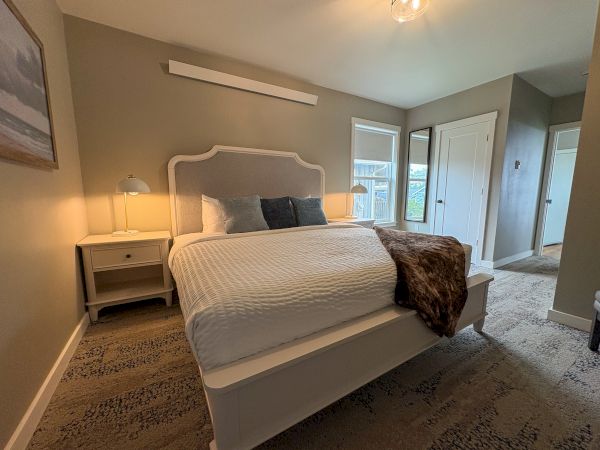 A cozy bedroom with a large bed, nightstand lamps, throw pillows, carpet, and French doors/windows to the outdoors.
